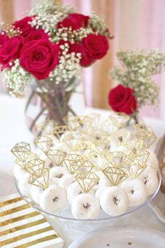 desserts and flowers on a table with red roses in vases behind the plate