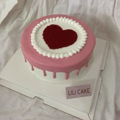 a heart shaped cake sitting on top of a white tablecloth covered bed sheet with the words lil cake written below it