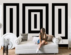 a woman sitting on top of a couch in front of a black and white wall