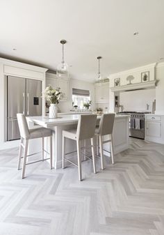 a kitchen with white cabinets and wooden floors is pictured in this image, there are four chairs at the center of the table