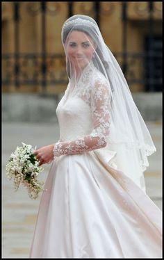 the bride is walking down the street in her wedding dress and veil with flowers on it