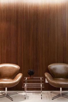 two brown leather chairs sitting next to each other in front of a wooden paneled wall