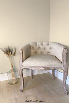 a white chair sitting on top of a wooden floor next to a vase filled with flowers