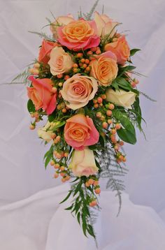 a bridal bouquet with peach roses and greenery on a white cloth background,