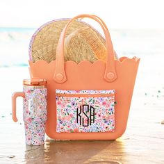 an orange purse and straw hat sitting on the beach next to a cup with a straw in it