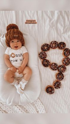 a baby is laying on a pillow next to some donuts and a knitted hat