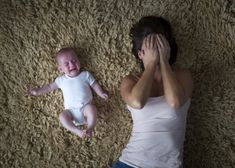 a woman laying on the floor next to a baby who is covering their eyes with her hands