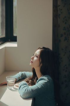 a woman sitting at a window sill with a glass in her hand and looking out the window