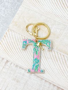 a gold keychain with a pink and green letter t on it