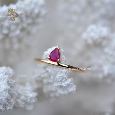 a gold ring with a pink stone on it sitting on some white snow covered rocks