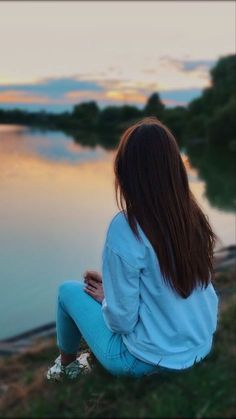 a woman sitting on the edge of a cliff looking out over a body of water