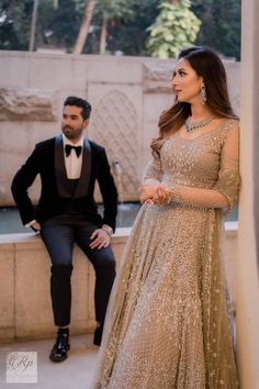 a man and woman in tuxedos standing next to each other near a fountain