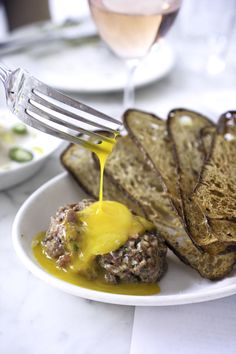 a white plate topped with bread and meat covered in gravy next to a glass of wine