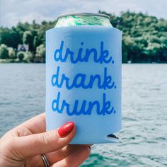 a woman holding up a can of drink in front of the water