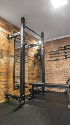 an empty gym room with squat racks and benches on the floor in front of a brick wall