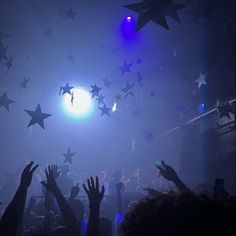 many people are reaching their hands up in the air at a concert with stars hanging from the ceiling