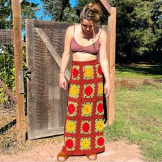 a woman standing in front of a wooden fence wearing a crocheted skirt with flowers on it