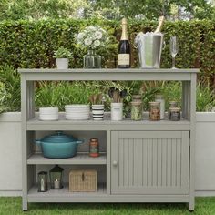 an outdoor bar with bottles and glasses on it's shelf, surrounded by greenery