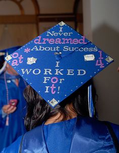 a woman wearing a blue graduation cap with words written on it and other people standing in the background