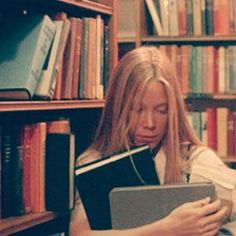 a woman sitting in front of a bookshelf holding a book and looking at it