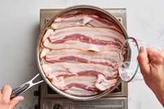 a pan filled with bacon sitting on top of a stove next to a person holding a spoon