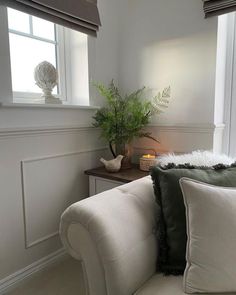 a white couch sitting in front of a window next to a table with a vase on it