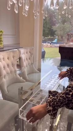 a woman sitting at a glass table in front of a couch and chandelier