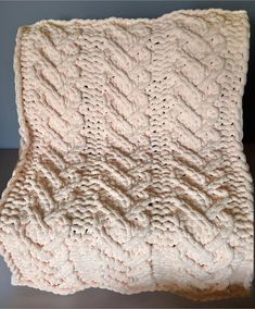 a white crocheted blanket sitting on top of a wooden table next to a wall