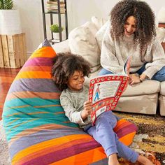 a woman and child sitting on a bean bag chair looking at a book in front of them