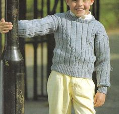 a young boy leaning against a pole wearing a sweater and pants with yellow pleated shorts