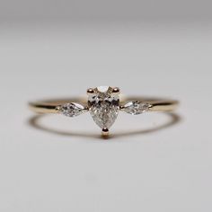 an engagement ring with three pear shaped diamonds on the side, set in yellow gold