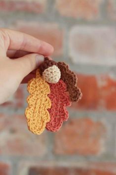 crocheted leaves are being held in front of a brick wall and someone is holding them