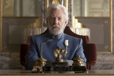 an older man sitting at a desk in front of a mirror wearing a blue suit