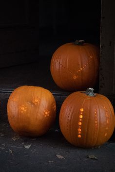 three orange pumpkins sitting on the ground in front of a door with light coming through them