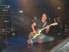 a man sitting on the floor with a guitar in his hand and people behind him