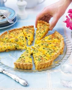 a person picking up a piece of quiche from a plate with flowers in the background