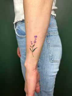 a woman's arm with a small purple flower tattoo on the left side of her arm