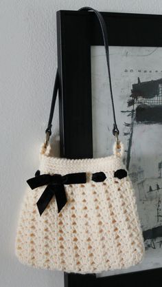 a white crocheted purse hanging on a wall next to a black frame with a painting in the background