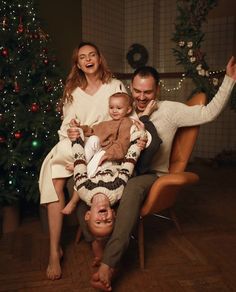 a man and woman holding a baby in front of a christmas tree with two other people