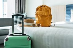 a yellow backpack sitting on top of a bed next to a green suitcase