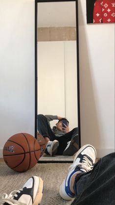 a man laying on the floor in front of a mirror with his feet up next to a basketball