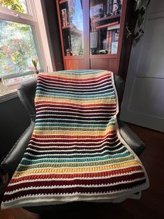 a multicolored crocheted blanket sitting on top of a black leather chair