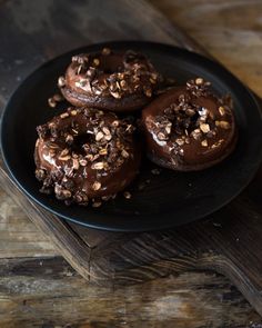 three chocolate donuts on a black plate topped with nuts and sprinkles