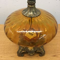 a large yellow glass vase sitting on top of a wooden table next to a wall