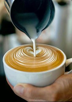 a person pouring milk into a cup of coffee