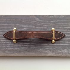 a brown leather belt with brass fittings on a wooden board or shelf, ready to be used as a tie bar