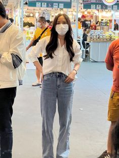 three people wearing face masks in an indoor shopping mall, one woman is standing and the other man is looking at her phone