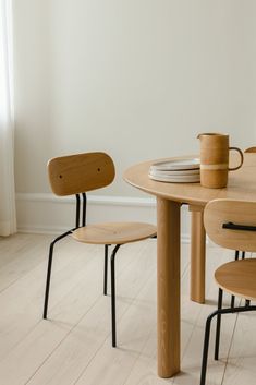 a wooden table with two chairs and a coffee cup on it, in front of a white wall