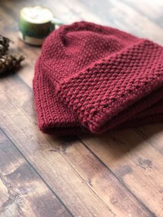 a red knitted hat sitting on top of a wooden floor next to pine cones