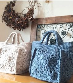 two crocheted bags sitting on top of a wooden table next to a wreath